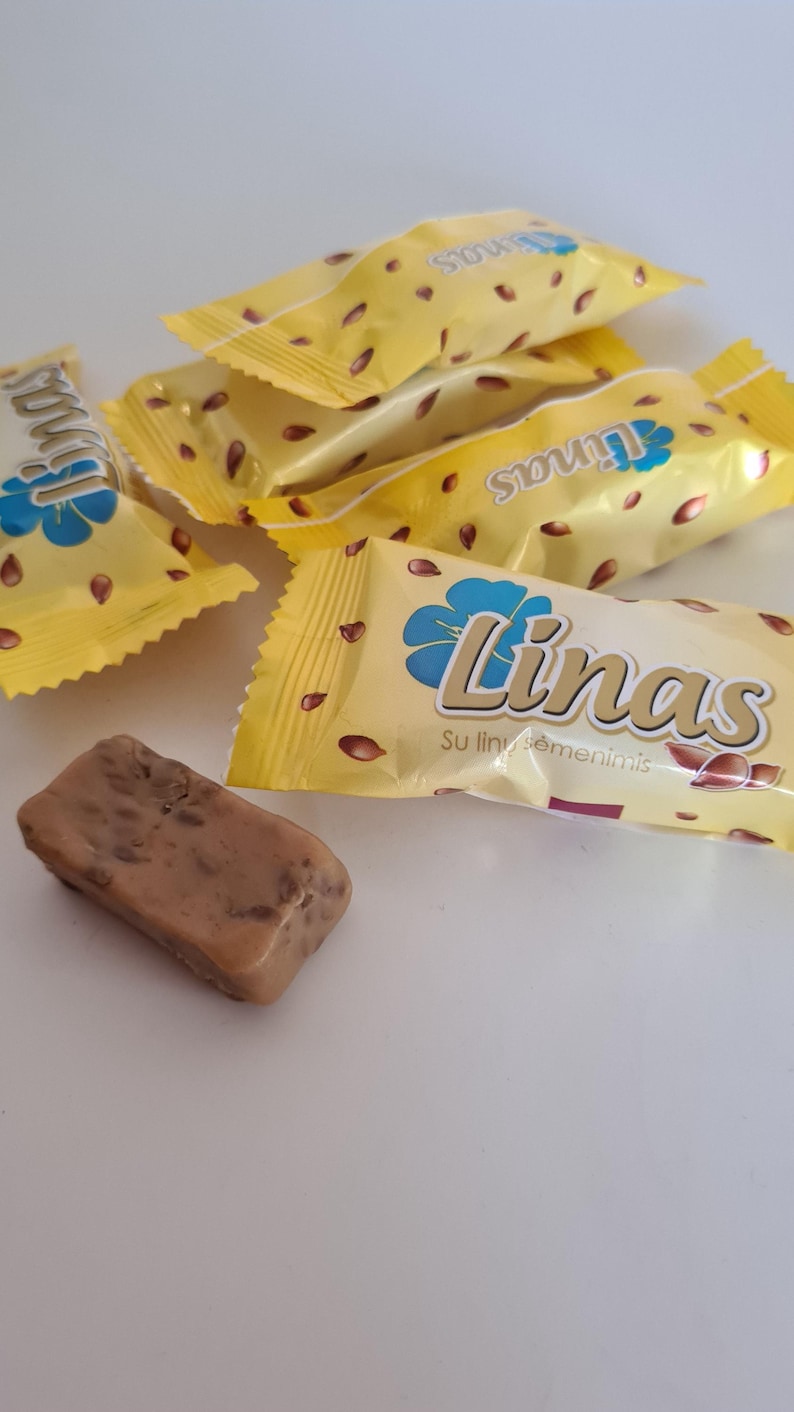 May include: Several individually wrapped candy bars with a light yellow wrapper and the word "Linas" in a stylized font. The wrappers have a floral design and scattered brown seeds. One unwrapped candy bar is visible.
