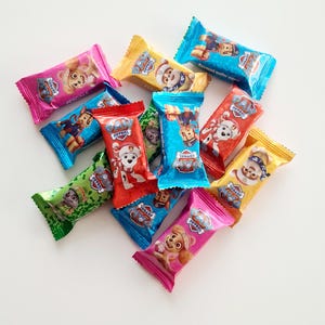May include: A collection of individually wrapped candy bars featuring characters from the Paw Patrol animated series. The wrappers are various colors, including pink, blue, yellow, green, and red, with the Paw Patrol logo.