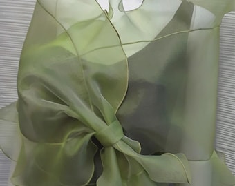 May include: A light green, sheer organza wrap with ruffled edges and a bow detail. The wrap is draped over a mannequin, showcasing its flowing design. The garment appears to be a formal wear accessory.