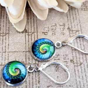 May include: A pair of round, silver-toned leverback earrings. Each earring features a vibrant, circular design with a blue and green spiral pattern. The earrings are displayed on a background with musical notes and a white flower.