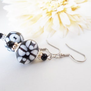 May include: Dangle earrings with black and white patterned beads. The beads have a floral design and are accented with small black beads and silver-tone metal findings. The earrings have a hook closure.