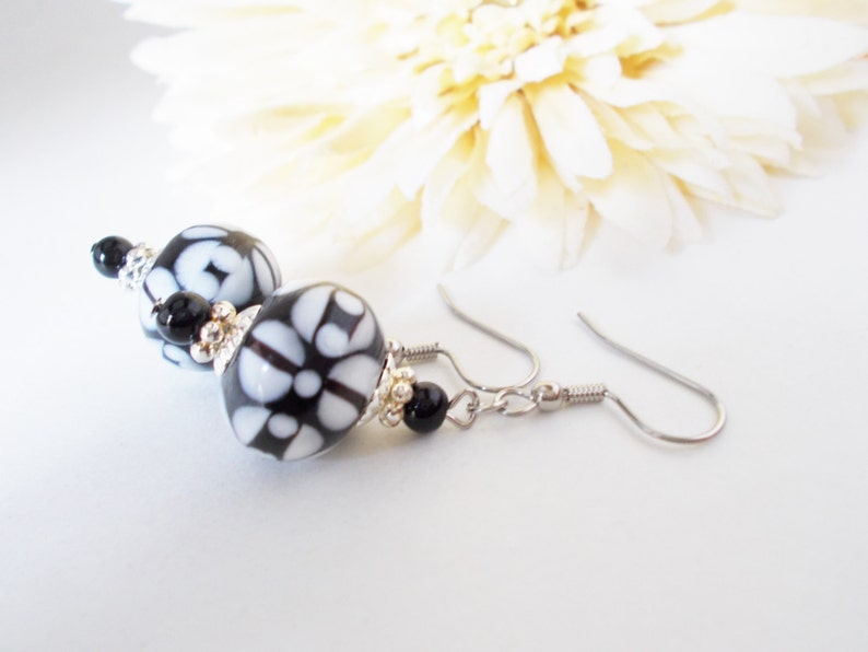 May include: Dangle earrings with black and white patterned beads. The beads have a floral design and are accented with small black beads and silver-tone metal findings. The earrings have a hook closure.
