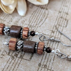 May include: Handmade earrings with dark and light brown wooden beads, silver-coloured metal beads, and small dark red beads. The earrings are suspended from silver-coloured ear wires.