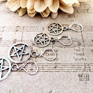 May include: Silver-colored pentagram charms and earring findings. The charms feature a five-pointed star within a circle. The earring findings have a lever-back closure. The items are displayed on a vintage sheet music background.