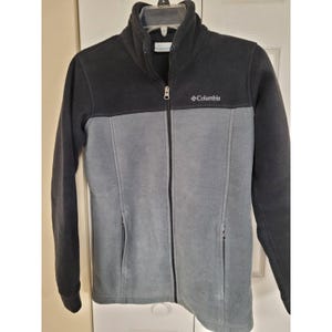 May include: A black and gray Columbia fleece jacket with a full zipper closure. The jacket has a high collar and two front pockets. The Columbia logo is embroidered on the chest.