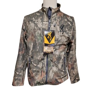 May include: Camouflage pattern jacket with a full zipper, featuring the Browning logo. The jacket has a high collar and two side pockets. A tag with the Browning logo and "A-TACS CAMO" is attached.