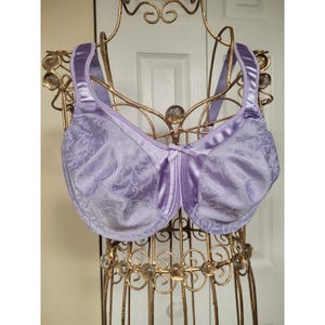 May include: A lavender underwire bra featuring a tonal damask pattern across the cups and wide, satin-finish shoulder straps. The garment includes a small center bow detail and structured cups with visible seams, providing full coverage support.
