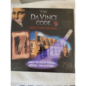 Puede incluir: Un rompecabezas en caja titulado "The Da Vinci Code: Rosslyn Chapel Revealed". La caja presenta imágenes de la capilla, un retrato y una linterna. El rompecabezas incluye 750 piezas y es para mayores de 10 años.