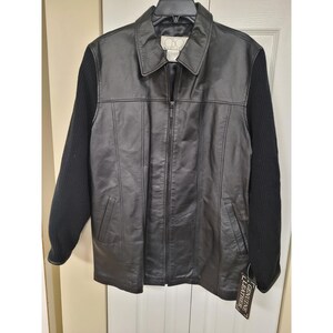 May include: Black leather jacket with black knit sleeves. The jacket has a collared neckline, a zipper closure, and two front pockets. A tag that says "GENUINE LEATHER" is attached to the jacket.