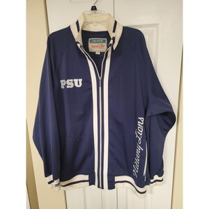 May include: Navy blue zip-up jacket with white stripes and accents. Features the letters "PSU" on the left chest and "Nittany Lions" in script on the right sleeve. The jacket has a white collar and cuffs.