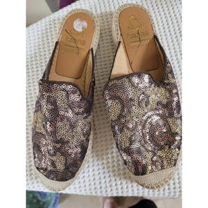 May include: A pair of Kanna espadrille slip-on shoes. The shoes feature a brown and gold sequined upper, a tan insole, and a beige woven sole. The brand name "Kanna" is visible on the insole.