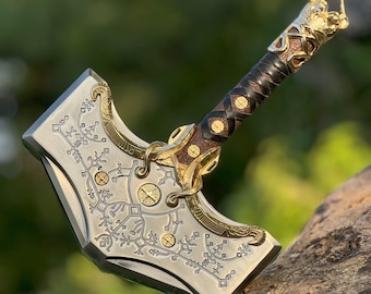May include: A detailed, silver-colored hammer with gold accents and intricate engravings. The handle is wrapped in dark brown leather with gold studs. The hammer's head features a decorative design.