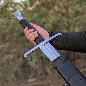 May include: A medieval-style sword with a polished steel blade and a black leather-wrapped handle. The sword has a crossguard and is partially sheathed in a black leather scabbard. The handle is approximately 6 inches long.