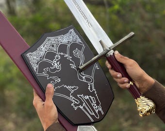 May include: A longsword with a silver blade featuring engraved text, a maroon handle, and a gold lion head pommel. The sword is paired with a black shield-shaped plaque displaying a white lion graphic and a maroon scabbard with a silver tip.