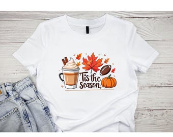 May include: White t-shirt with a fall-themed graphic. The design includes a coffee cup with whipped cream, cinnamon sticks, a red maple leaf, a football, and a pumpkin. Text reads "Tis the Season."