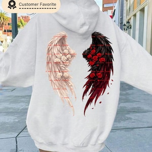 May include: White hoodie featuring a design of angel and demon wings on the back. The angel wing is white with cream-colored roses, while the demon wing is black with red roses. The hoodie has a hood and long sleeves.