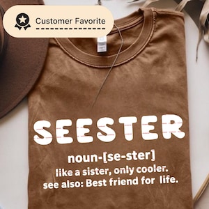 May include: A brown t-shirt with the word "SEESTER" in large white letters. Below the word is a definition: "noun-[se-ster] like a sister, only cooler. see also: Best friend for life." A "Customer Favorite" badge is visible.