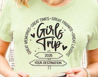 May include: A light green t-shirt with the words "Girls Trip" in a cursive font, surrounded by the phrases "Great Times," "Great Friends," "Great Memories," and "Great Laughs." Below the text are directional signs with "2026" and "Your Destination."