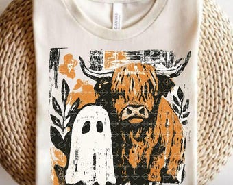 May include: Cream-colored t-shirt featuring a distressed graphic of a Highland cow and a ghost. The cow is in shades of orange and black, with a ghost to the left. Floral and leaf accents surround the cow and ghost.