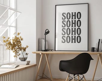 May include: A minimalist home office setup featuring a wooden desk, black chair, and a framed print that reads "SOHO" multiple times. The room is bright with natural light, and includes a vase of dried flowers.