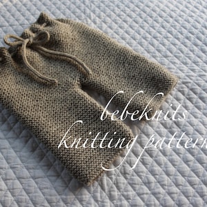 Puede incluir: Patrón de tejido para pantalones de bebé. Los pantalones son beige y tienen un cordón. El texto "bebeknits knitting pattern" es visible en la imagen.