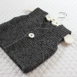 May include: A grey knitted waistcoat with a white button. The waistcoat is hanging on a white wooden hanger.