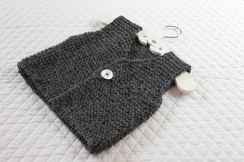 May include: A grey knitted waistcoat with a white button. The waistcoat is hanging on a white wooden hanger.