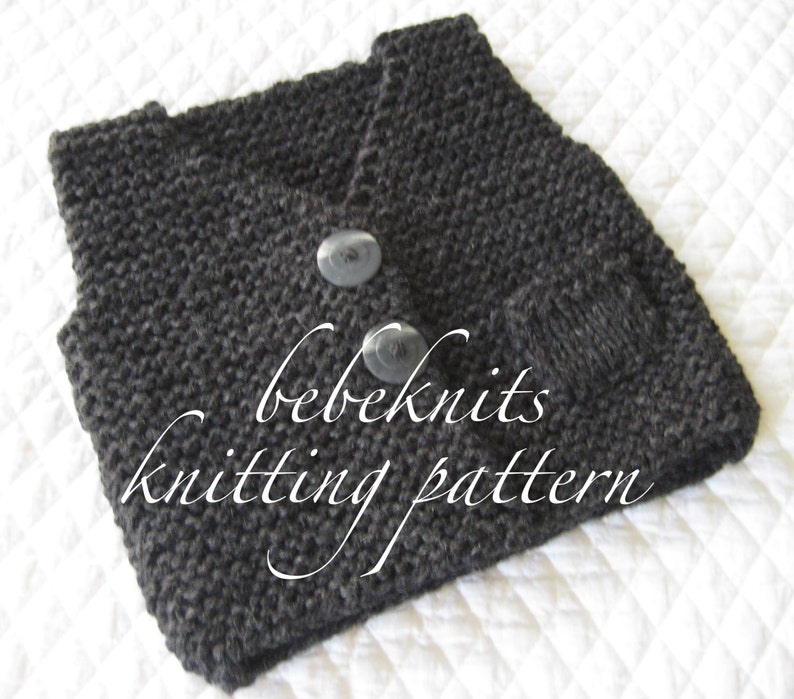 Pode incluir: Um colete de malha cinzento escuro para beb&eacute; com dois bot&otilde;es pretos. O colete est&aacute; dobrado e tem uma etiqueta que diz "bebeknits knitting pattern".