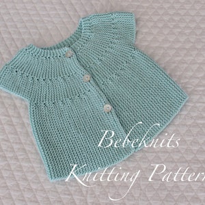 May include: A light blue knitted baby cardigan with short sleeves and button closures. The cardigan has a simple stitch pattern and is laid flat on a white quilted surface. The text "Bebeknits Knitting Pattern" is visible in the bottom right corner of the image.