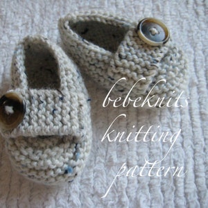 May include: A pair of white knitted baby booties with a button closure. The booties have a speckled pattern and are made with a soft yarn.