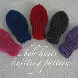 May include: Five pairs of knitted baby mittens in different colours: pink, red, blue, grey, and purple. The mittens are laid out on a white fluffy surface. The text "bebeknits knitting pattern" is written below the mittens.
