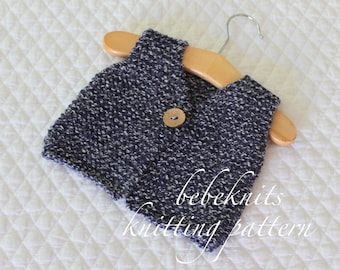 May include: A blue and white knitted waistcoat with a wooden button, hanging on a wooden hanger. The waistcoat is for a baby and has a "bebeknits knitting pattern" label.