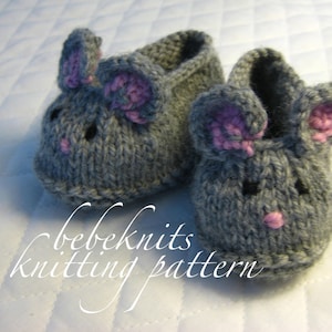May include: A pair of grey knitted baby booties shaped like mice with pink ears and noses. The booties have a "bebeknits knitting pattern" label.