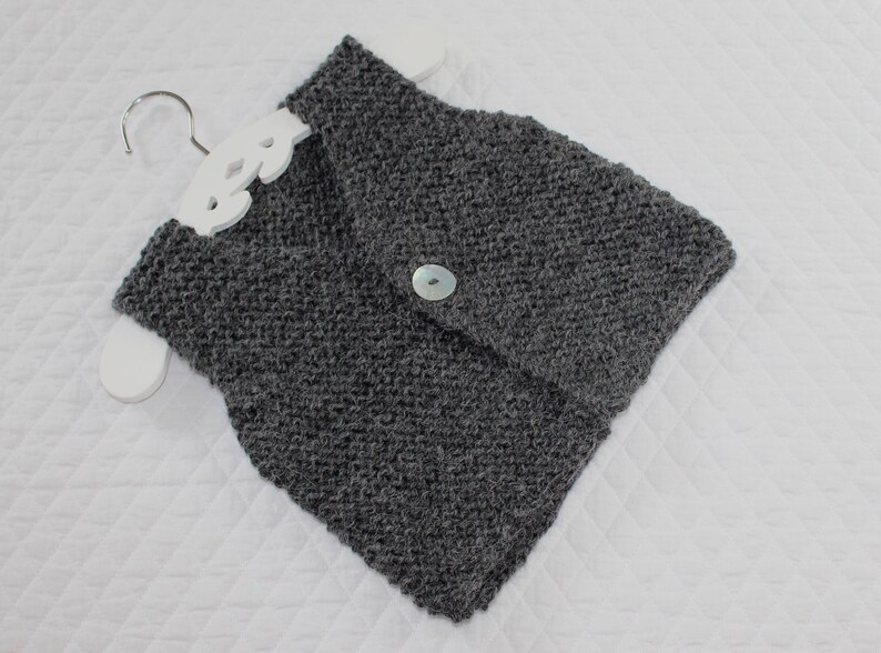 May include: A grey knitted cowl neck scarf with a single button fastening.