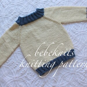 May include: A knitted baby sweater in cream with blue trim around the neck and sleeves. The sweater is laid flat on a white surface with the text "bebeknits knitting pattern" visible.