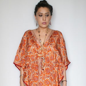 Op de afbeelding: Een lange, vloeiende oranje en rode geprinte kaftan met een V-hals en een strik in de taille. De kaftan is gemaakt van een zachte, zijdeachtige stof en heeft een ontspannen pasvorm.