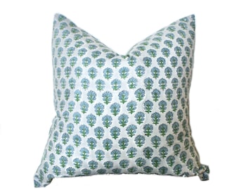 Puede incluir: Cojín decorativo cuadrado con fondo blanco y un patrón repetitivo de diseños florales azules y verdes. El cojín tiene un aspecto suave y acogedor, perfecto para añadir un toque de color y patrón a cualquier habitación.