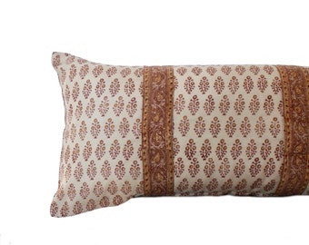 Puede incluir: Una almohada larga y rectangular con fondo blanco y un patrón floral marrón y naranja. La almohada tiene un borde decorativo con un diseño de paisley.