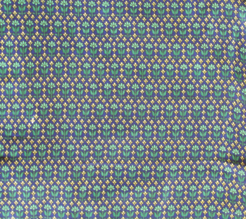 May include: A blue fabric with a repeating pattern of small green and yellow flowers.