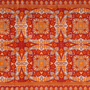 Op de afbeelding: Rode stof met een herhalend patroon van oranje en grijze bloemmotieven. De stof heeft een traditionele, sierlijke uitstraling.