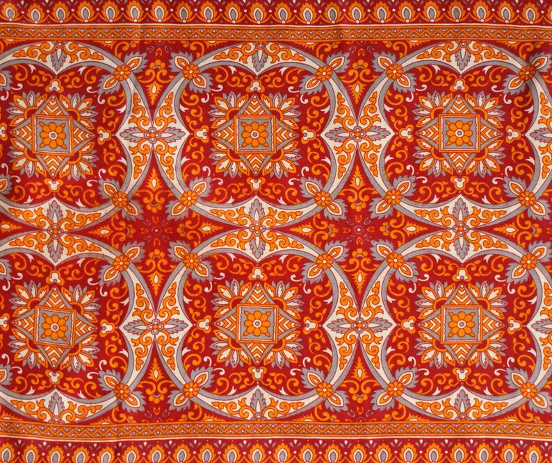 Op de afbeelding: Rode stof met een herhalend patroon van oranje en grijze bloemmotieven. De stof heeft een traditionele, sierlijke uitstraling.