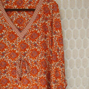 Op de afbeelding: Een lang mouw, oranje en witte bloemenprint kaftan met een V-hals en een trekkoord in de taille.