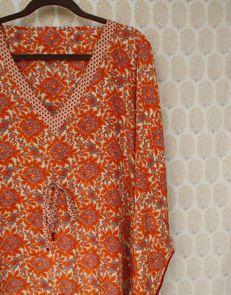 Op de afbeelding: Een lang mouw, oranje en witte bloemenprint kaftan met een V-hals en een trekkoord in de taille.