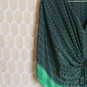 May include: A blue and green patterned kimono with a green trim. The kimono is hanging on a hanger against a white background with a floral pattern.