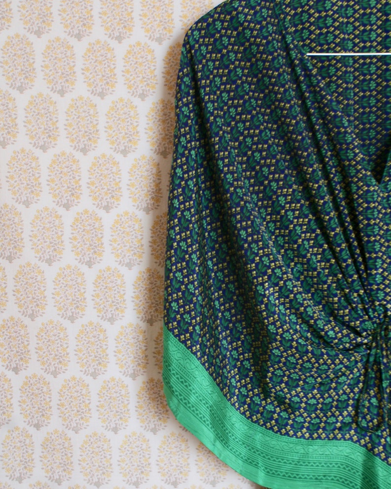 May include: A blue and green patterned kimono with a green trim. The kimono is hanging on a hanger against a white background with a floral pattern.