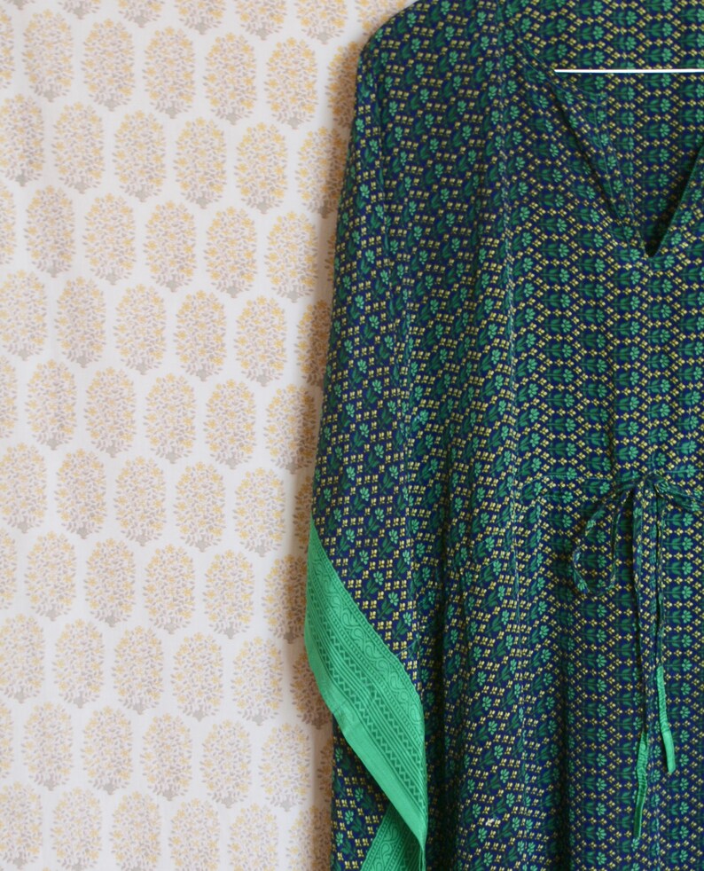 May include: A blue and green patterned kaftan with a green trim. The kaftan has a V-neck and a tie at the waist.