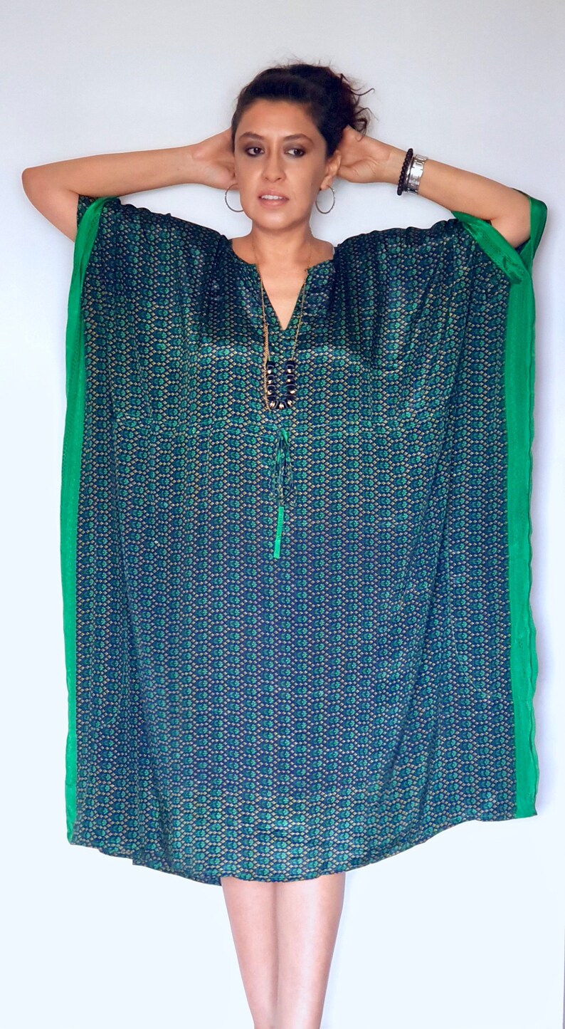 May include: A woman wearing a blue and green patterned kaftan with a green trim. The kaftan has a V-neck and a long, flowing silhouette.