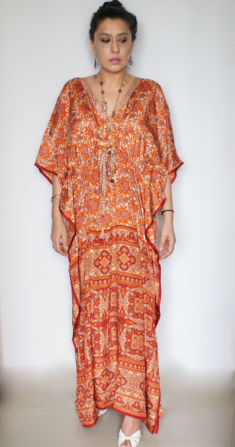 Op de afbeelding: Een lange, vloeiende oranje en rode geprinte kaftan met een V-hals en een strik in de taille. De kaftan is gemaakt van een zachte, zijdeachtige stof en heeft een ontspannen pasvorm.