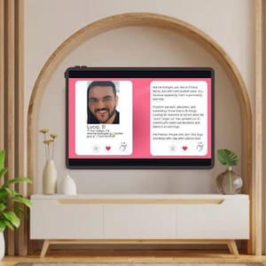 May include: A digital tablet shows a dating profile with a photo of a man named Luca, 31, and text. The profile is set against a pink background. The tablet is on a white cabinet with a wooden arch and wall in the background.