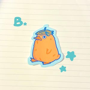 May include: An orange sticker of a cartoon duck-like creature with a leaf hat and blue outline. The sticker has a light blue background with the letter "B" and two blue star shapes.